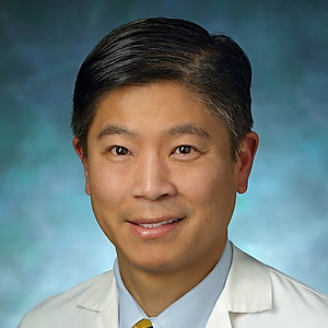 A headshot of Dr. Edward S. Chen wearing a white lab coat over a light blue button-down shirt. He has short, black hair parted to one side and is smiling. The background is a textured blue gradient.