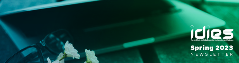 A teal and green toned image of a closeup laptop on a picnic table. There's glasses and a bunch of flowers next to it.