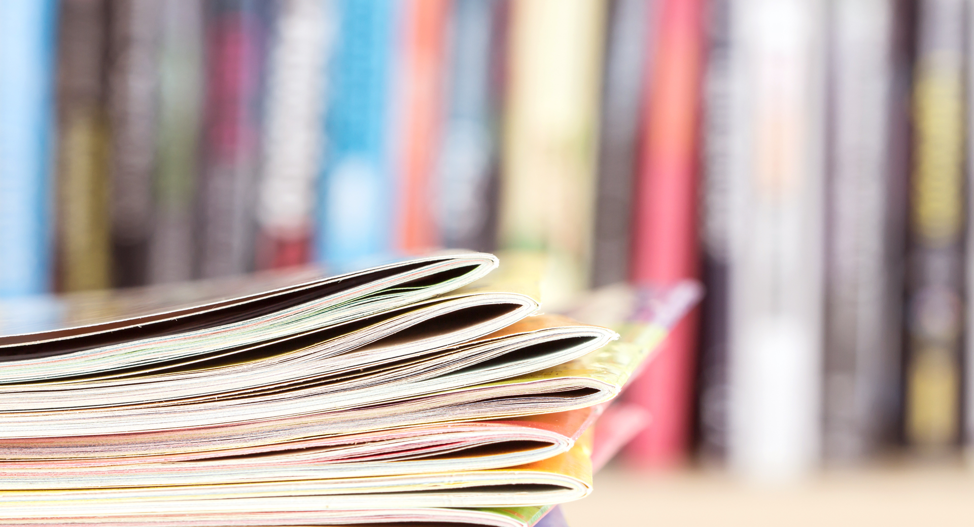 Close up edge of colorful magazine stacking with blurry bookshelf